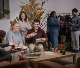 Narratieve fotografie voor het aantonen van samenwerken en praktijk leren in Leiden, met een teamoverleg aan tafel en op de achtergrond een kledingrek dat verwijst naar werk- en leerervaring in de stad. Groep mensen overlegt in een ruimte met koffie en papieren; op de achtergrond kiezen twee personen kleding uit een rek.